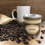 Coffee Candle next to a bag of spilled coffee beans and a white mug in the background.