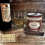 Whiskey candle sits in a wooden setting with a bottle and glass of whiskey next to it.