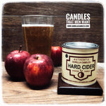 Hard Cider candle in a metal next to some apples and hard cider 